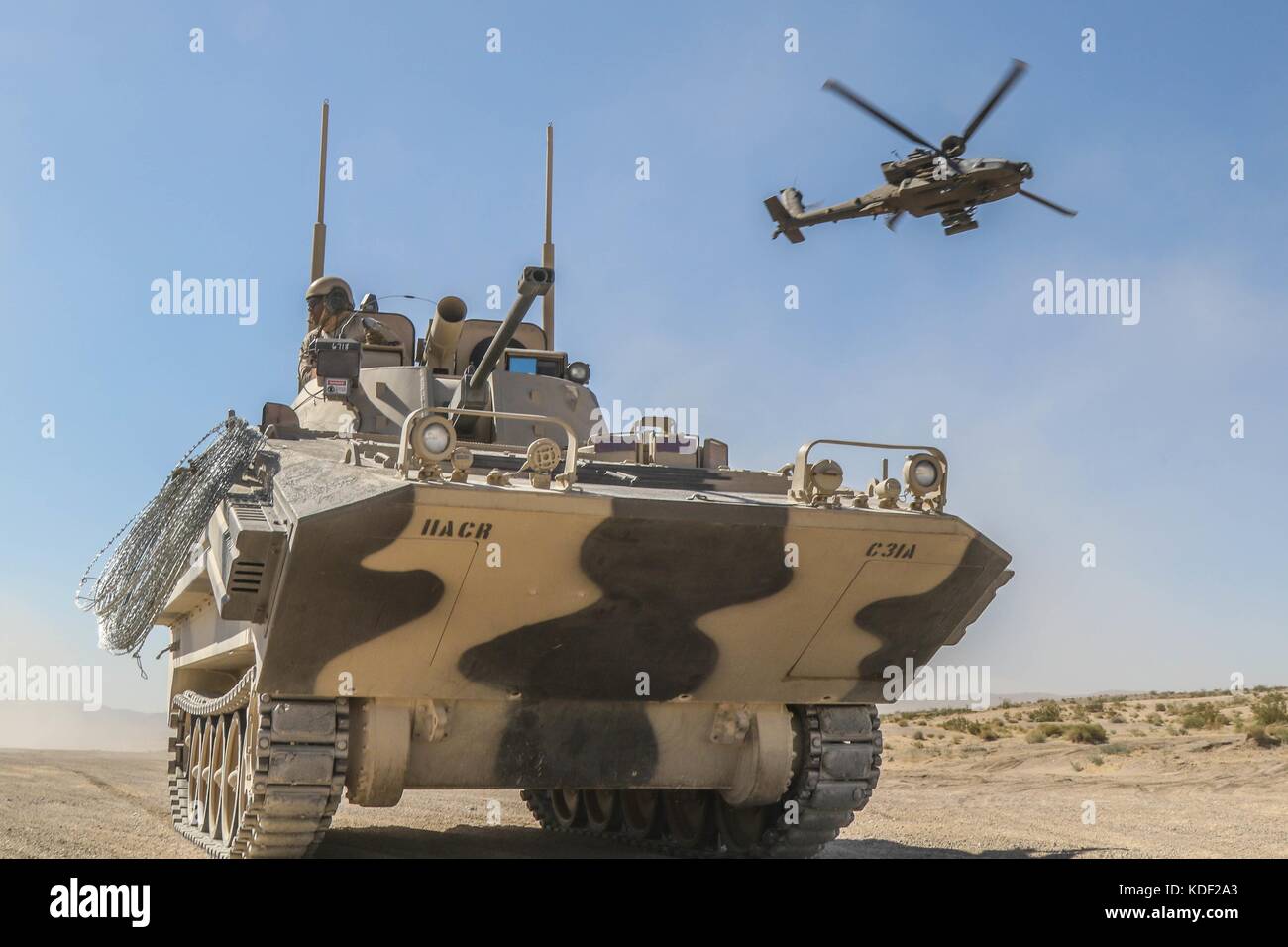 A U.S. Army AH-64 Apache attack helicopter flies over a Opposing Force Surrogate Vehicles designed to replicate Russian military armored vehicles during assault training near the John Wayne Foothills at the Fort Irwin National Training Center July 1, 2017 in Fort Irwin, California.   (photo by Austin Anyzeski via Planetpix) Stock Photo