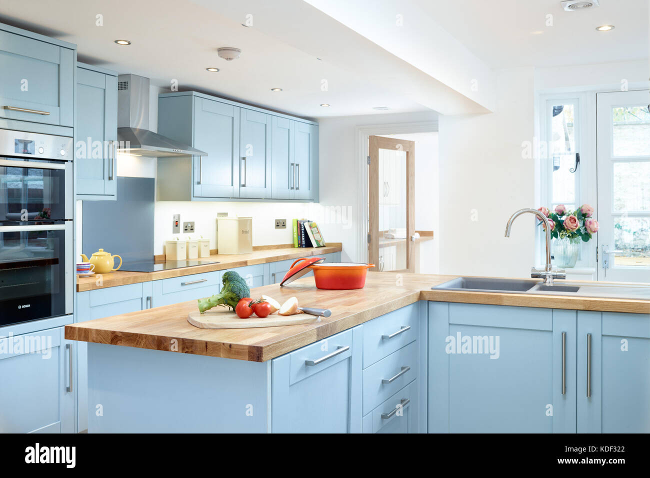 A new, modern, blue, shaker style designer kitchen showing cabinets, appliances and counter top. With some food preparation Stock Photo