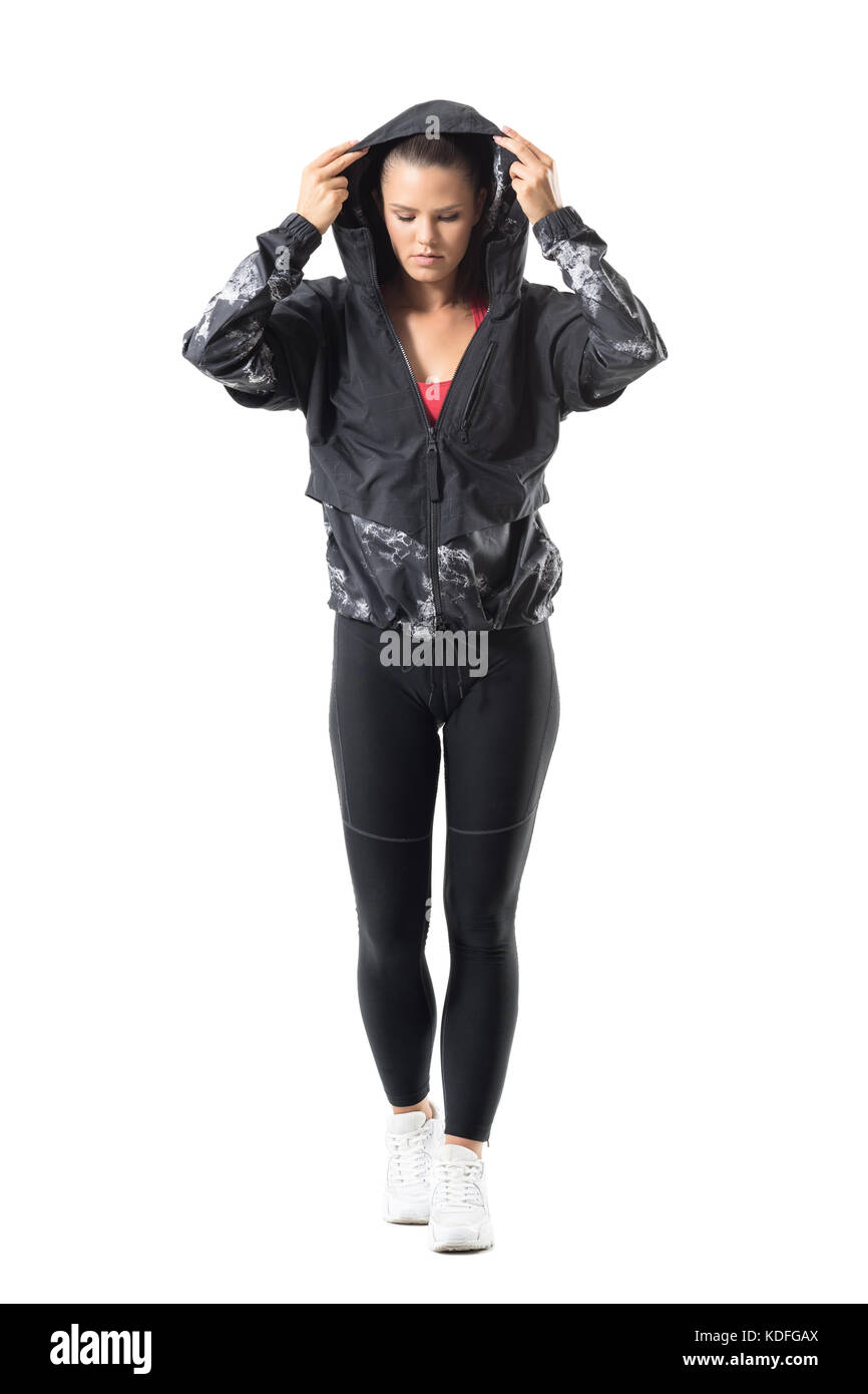 Front view of young active woman put on tracksuit jacket hoodie looking down. Full body length portrait isolated on white background. Stock Photo