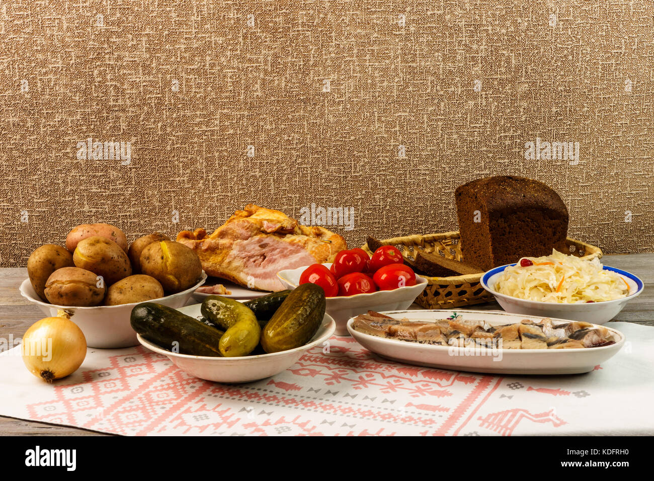 Ukrainian national dish is baked potatoes. Baked whole potatoes in skins with sauerkraut, salted herring, marinated red tomatoes and cucumbers Stock Photo