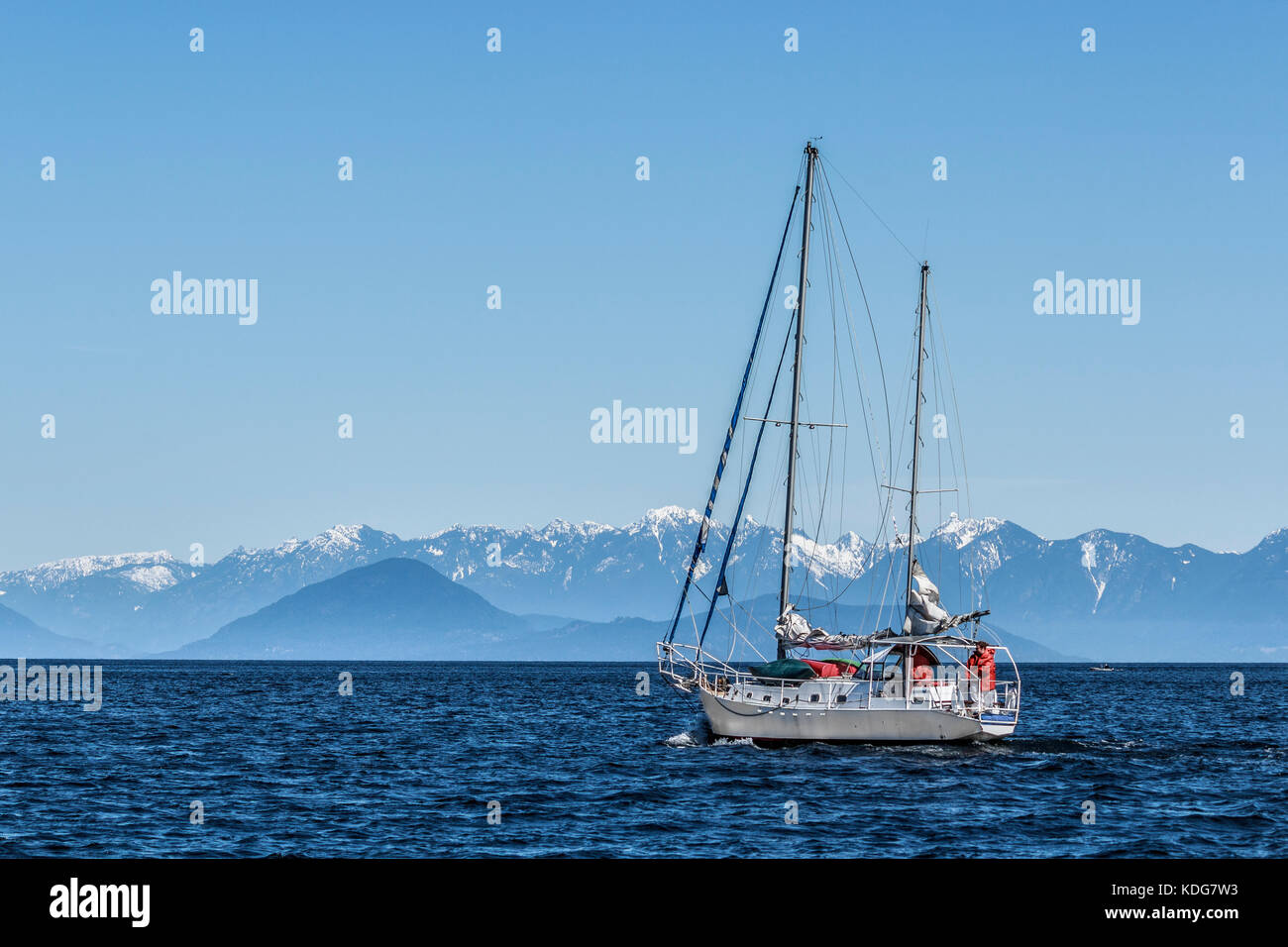 A sailboat sets out across BC's Strait of Georgia on a cold, clear day in early spring (Bowen Island, Howe Sound and Coast Range in background). Stock Photo