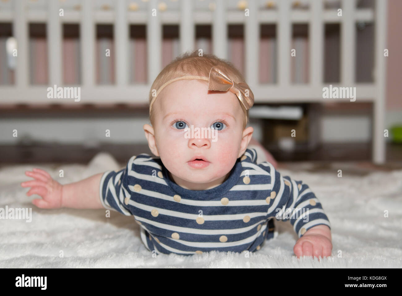 Baby Girl with Bow on Head Lying on Tummy with Crib in Background Stock