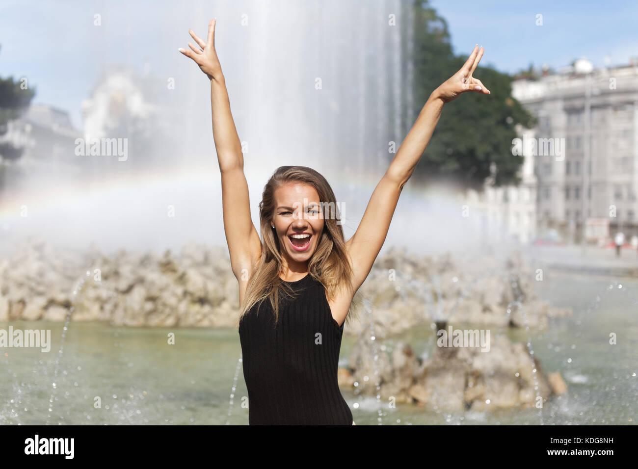 Young carefree woman hands up in the air at park fountain Stock Photo
