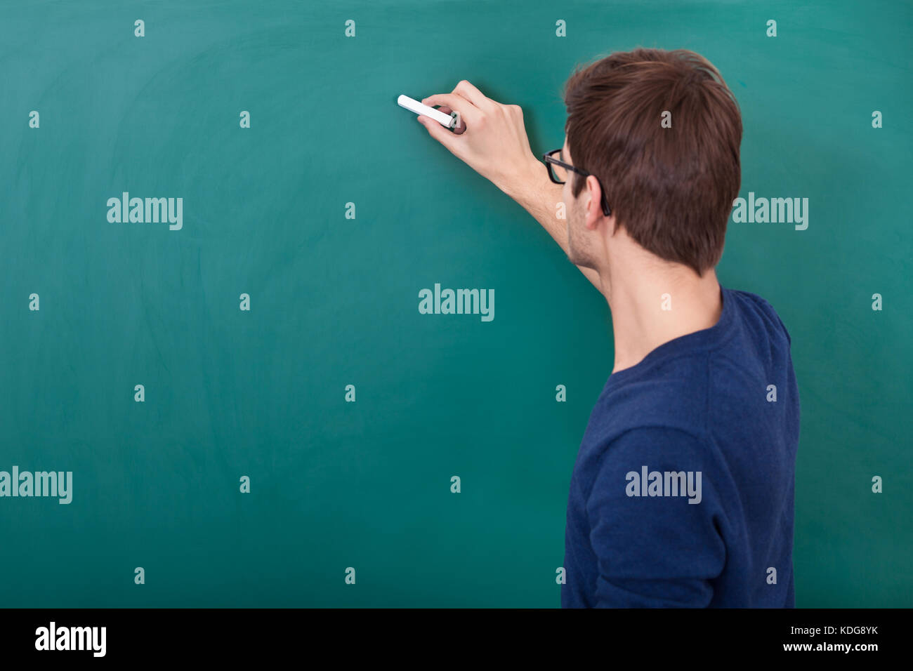 Rear View Of A Male Student Writing On Chalkboard With Chalk Stock Photo