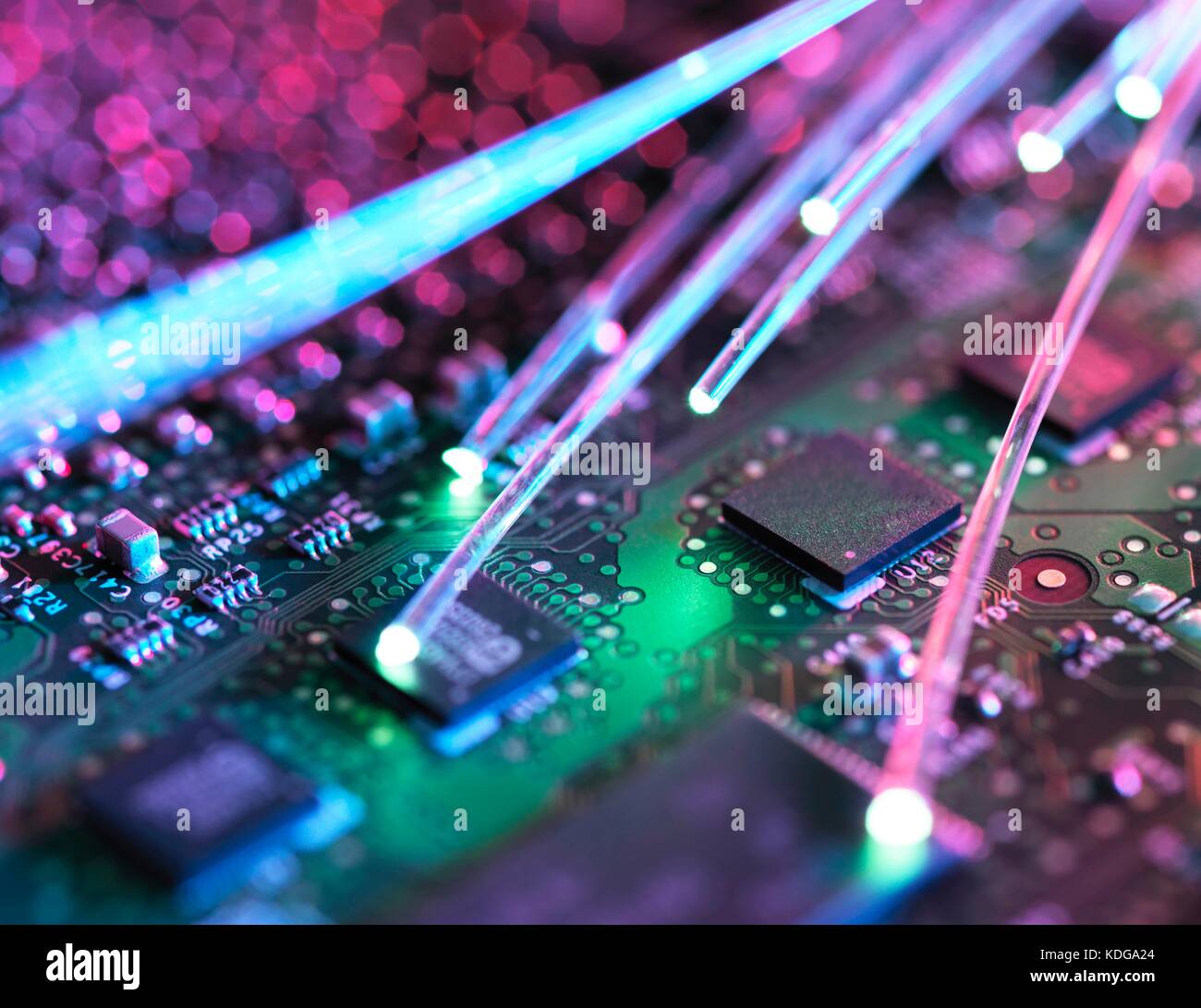 Fibre optic strands carrying data, with electronics in the background. Stock Photo