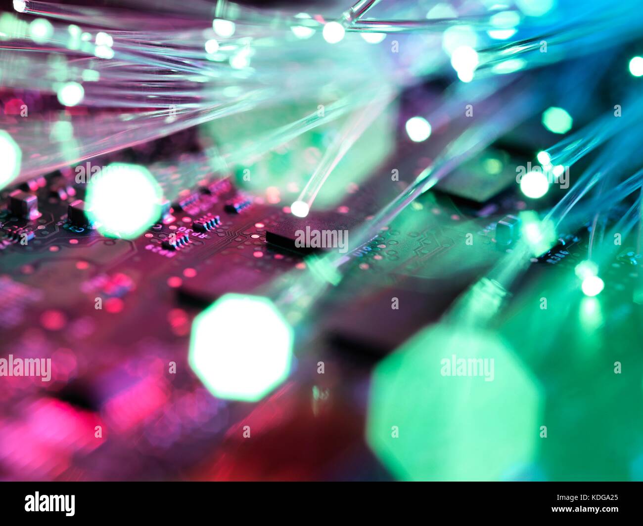 Fibre optic strands carrying data, with electronics in the background. Stock Photo