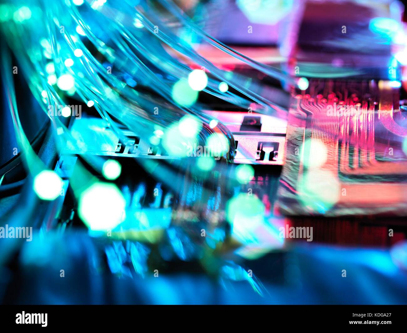 Fibre optic strands carrying data, with electronics of a laptop in the background. Stock Photo