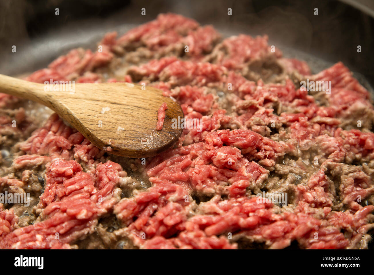 Minced meat being fried in a pan, wooden spatula lying in the pan and steam coming of the meat. Stock Photo