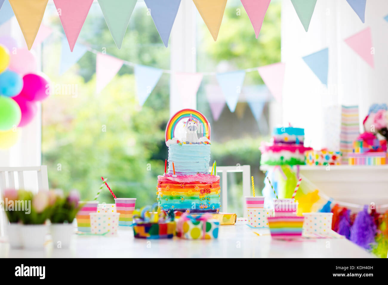 Kids birthday party decoration and cake. Decorated table for child birthday celebration. Rainbow unicorn cake for little girl. Room with festive ballo Stock Photo