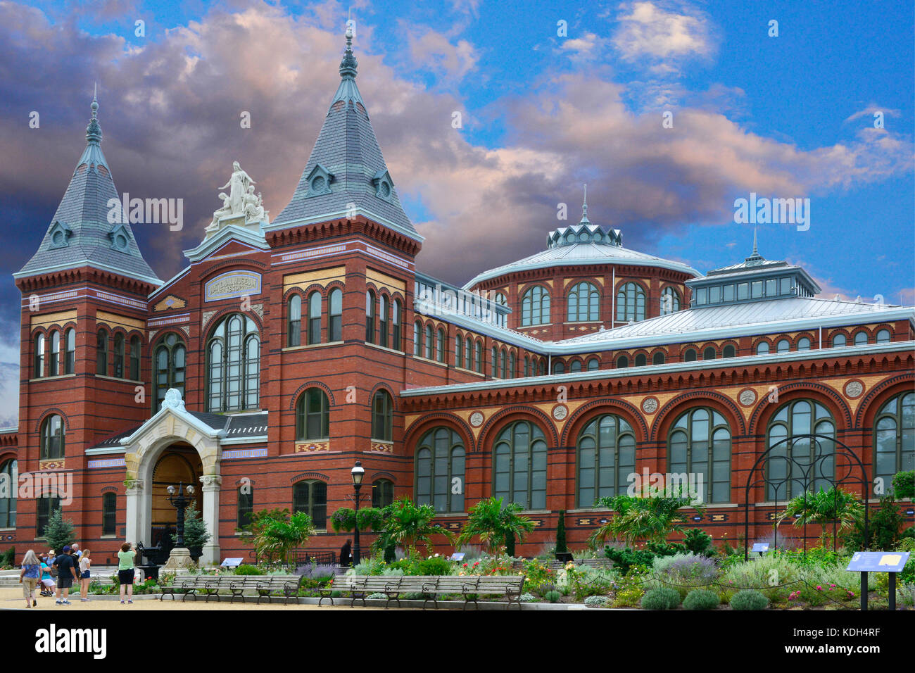 Tourists walk along the sidewalk of lovely landscaping and the historic red brick Smithsonian's Arts and Industries Building in Washington, DC, USA Stock Photo