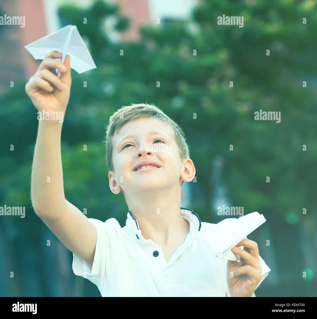 happy boy playing with simple paper airplane toy on sunny day in town ...