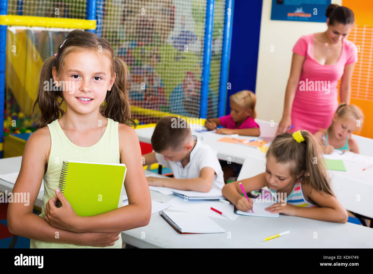 Cheerful schoolgirl standing with textbook in elementary school class ...