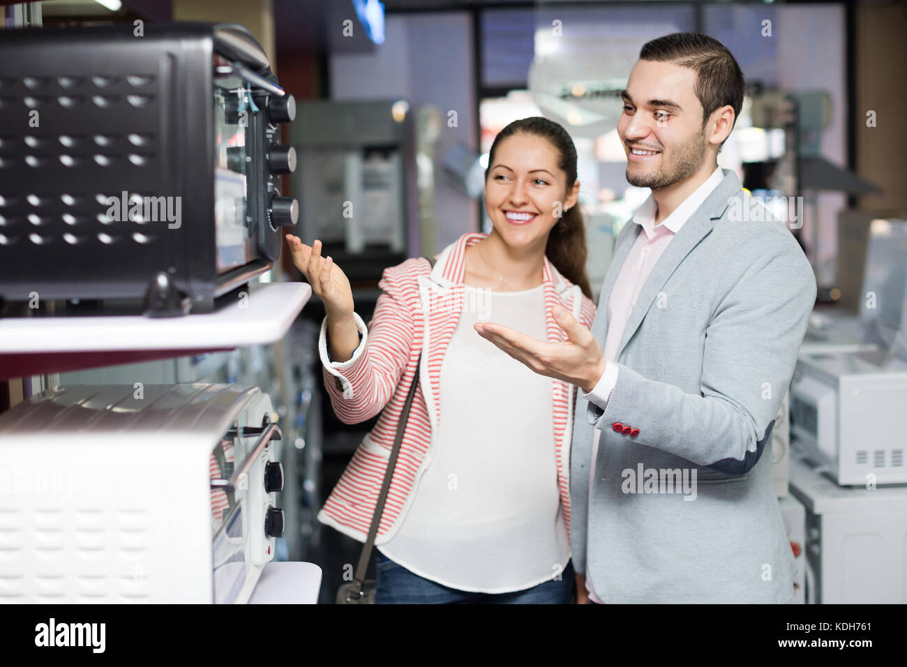 Positive smiling customers choosing new microwave oven in hypermarket . Focus on guy Stock Photo