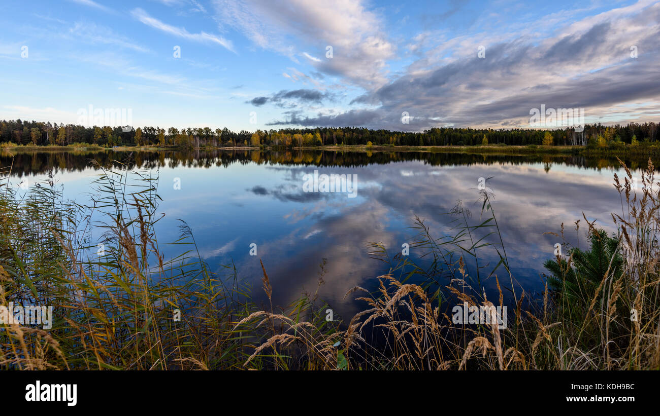 autumn colored trees on the shore of lake with reflections in water ...