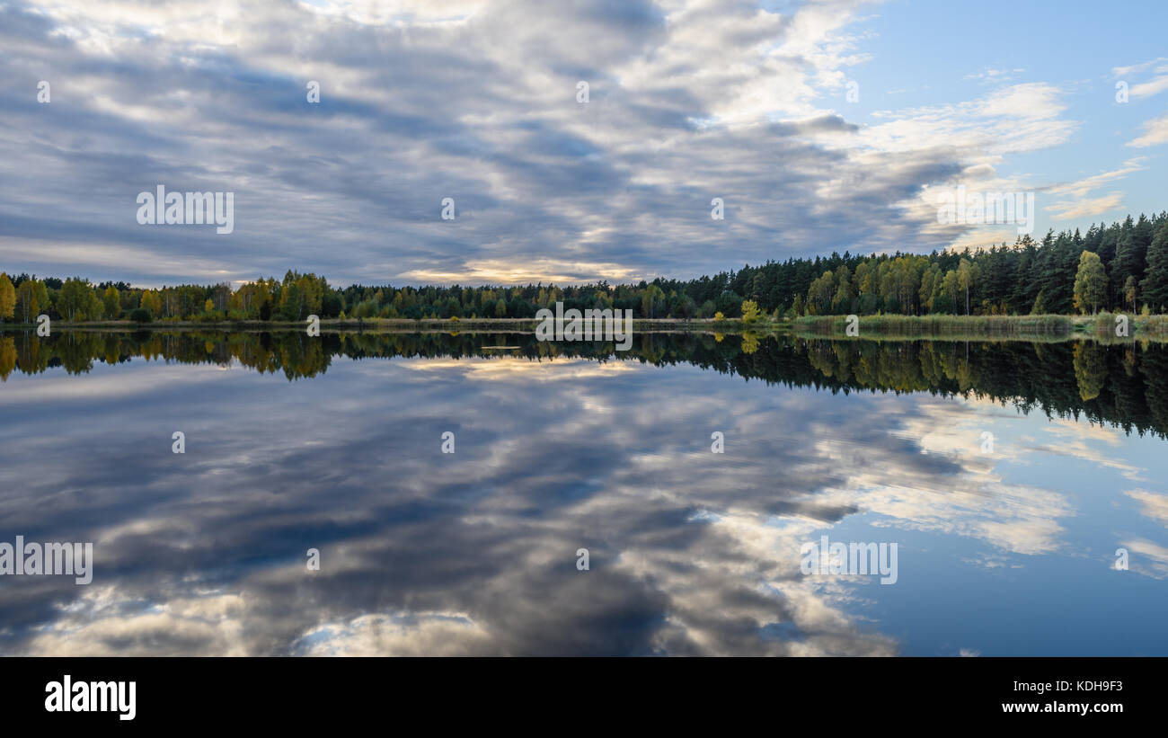 autumn colored trees on the shore of lake with reflections in water ...