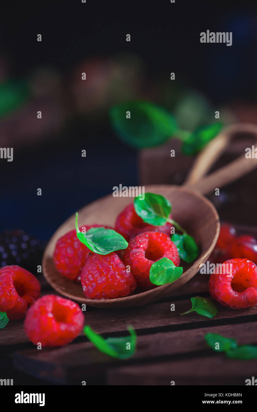 Summer still life with berries in a wide wooden spoon on a dark ...