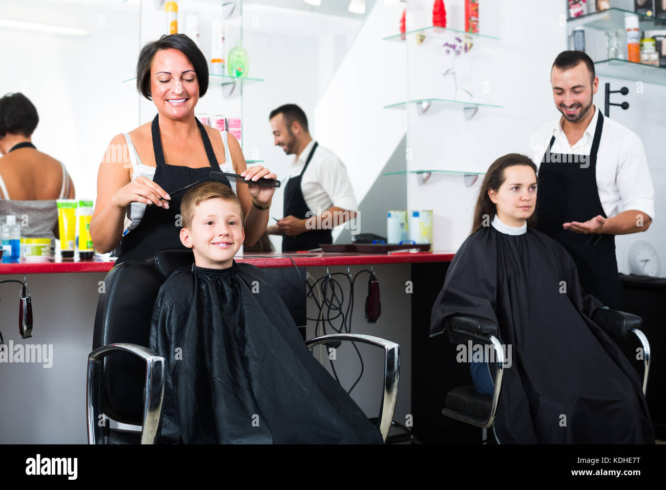 Smiling Female Hairdresser Cutting Hair Cute Boy In Elementary