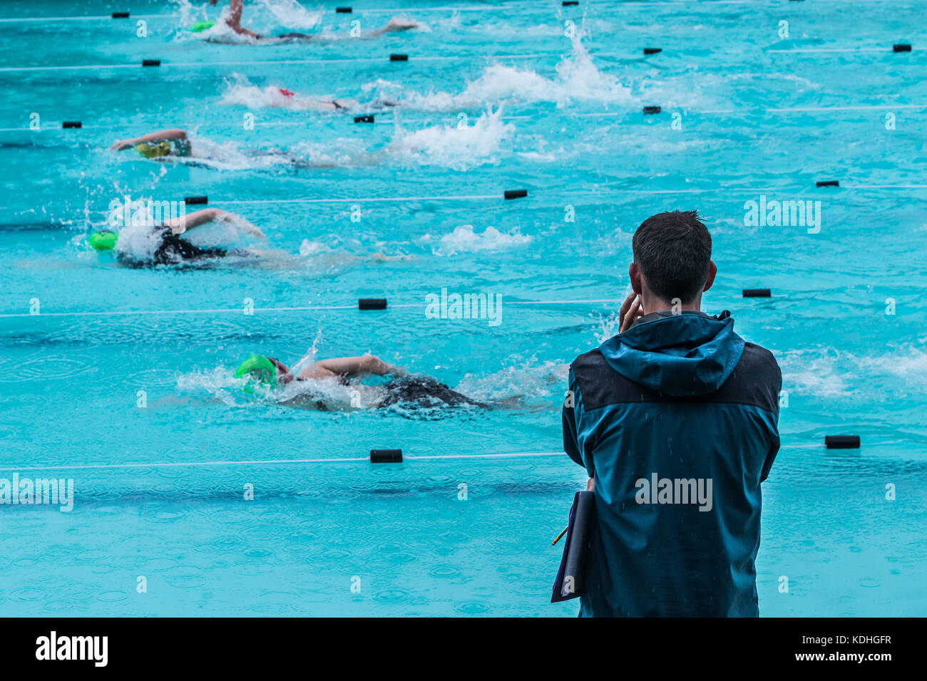 male swimming coach standing by the swimming pool in the rain watching