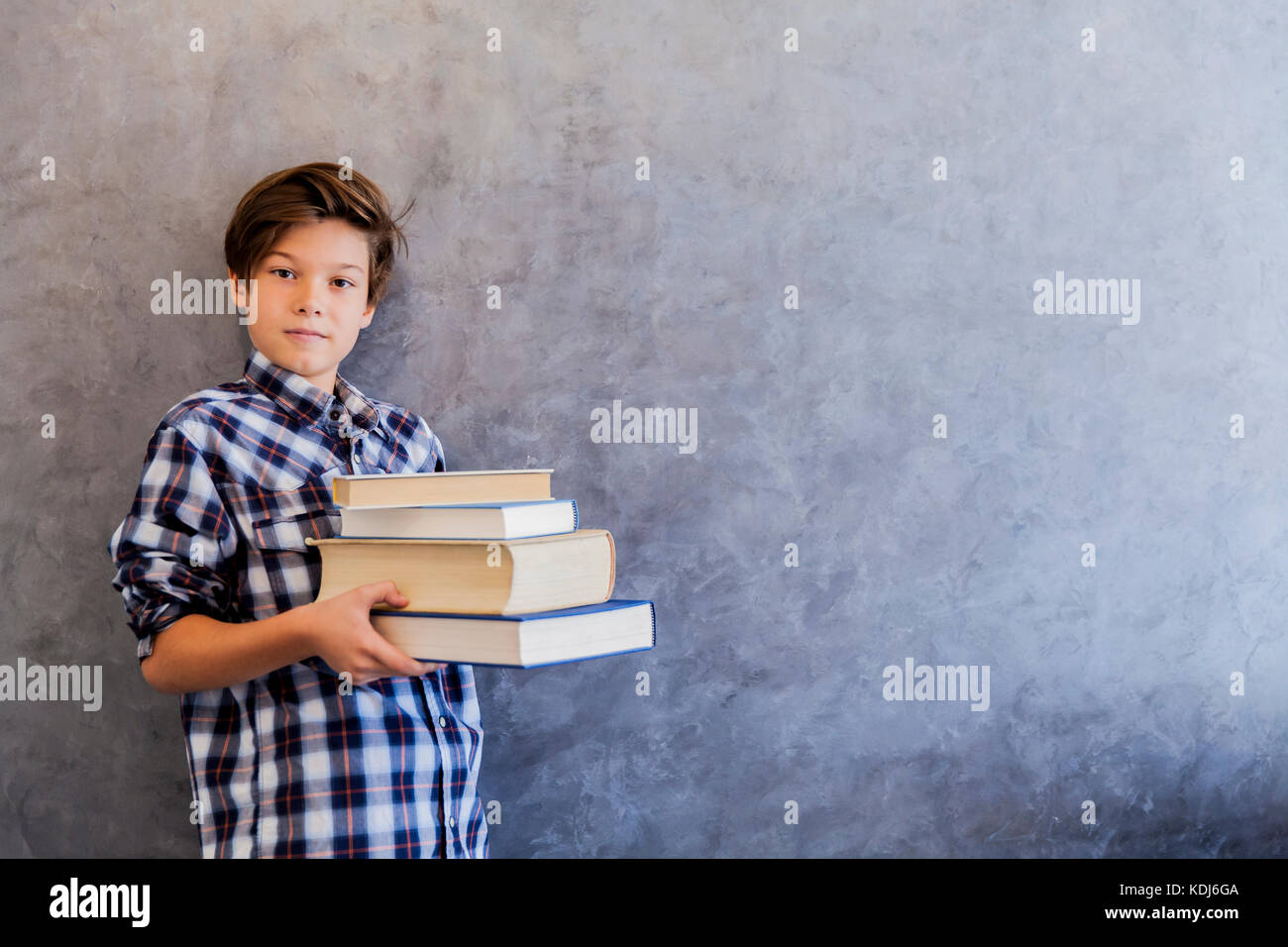 Cute teenage school boy holding books against wall Stock Photo - Alamy