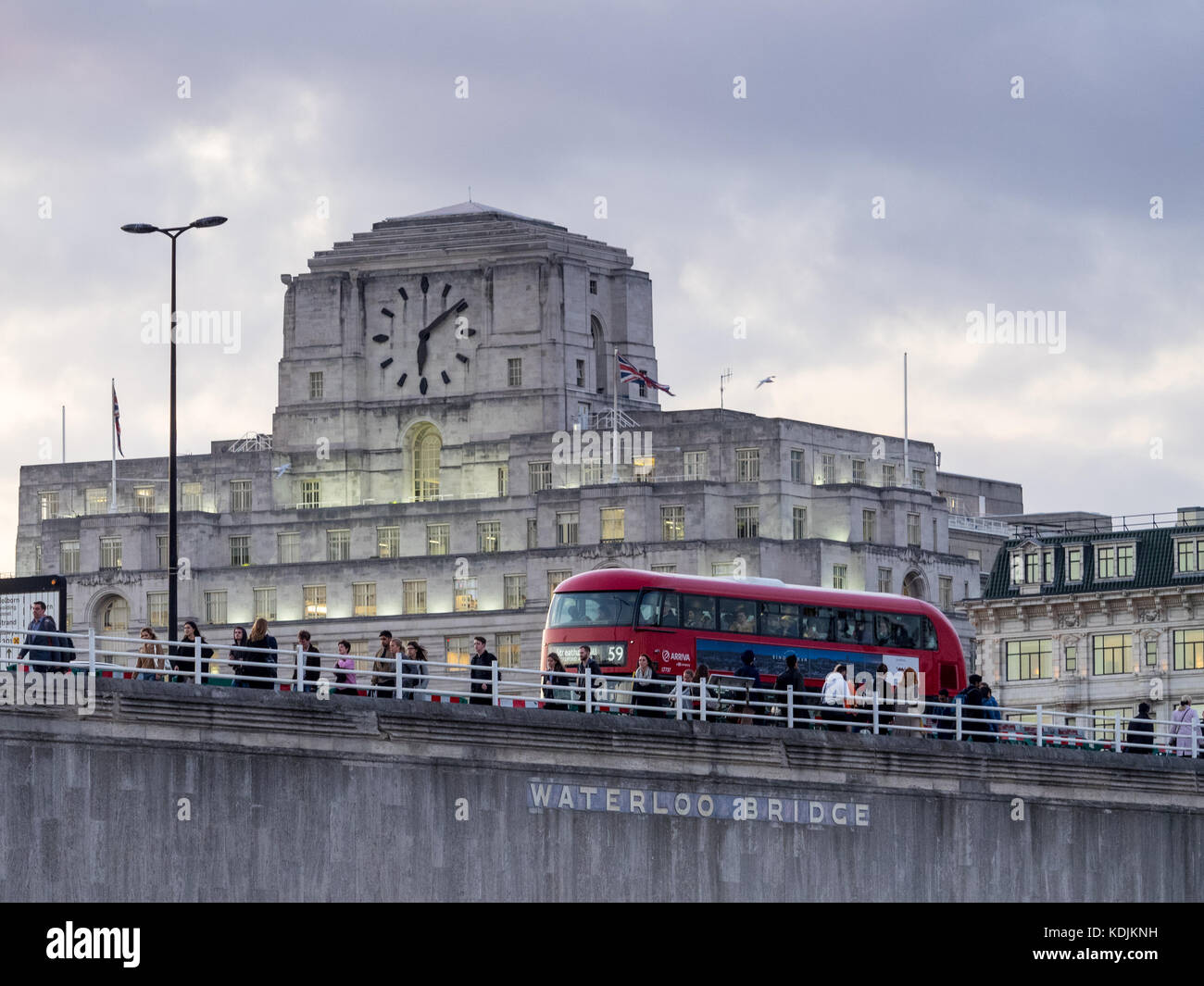 London Bus and commuters cross Waterloo Bridge in front of Shell Mex House in central London at dusk Stock Photo