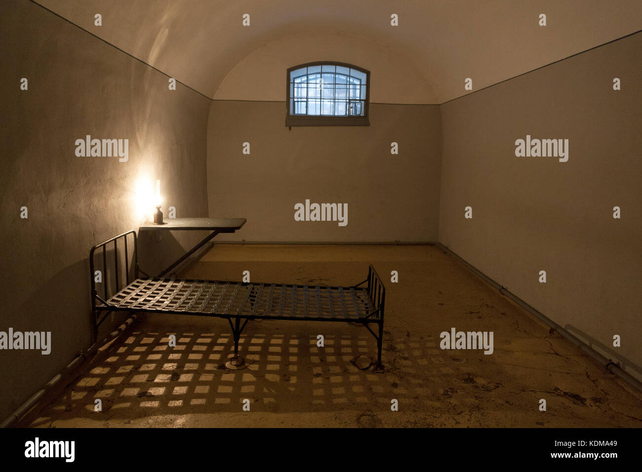 Old jail cell interior in the prison of Peter and Paul fortress in Saint Petersburg, Russia, with a little window, vintage lamp and iron bed. Stock Photo