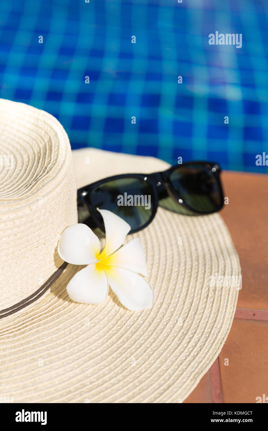 Sunglasses with flower and straw hat on border of a swimming pool ...