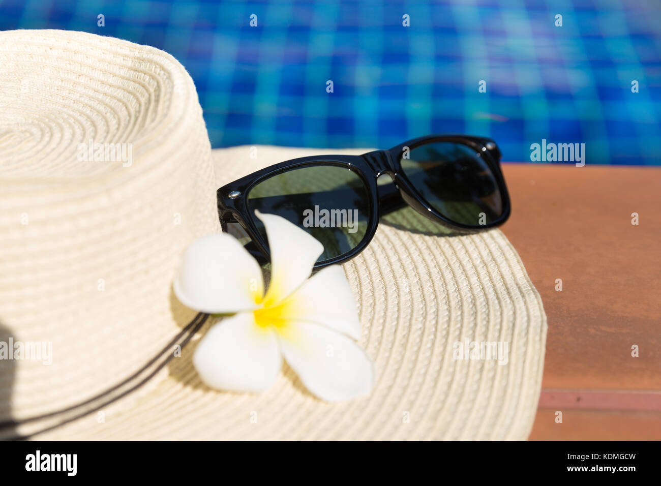 Sunglasses with flower and straw hat on border of a swimming pool ...