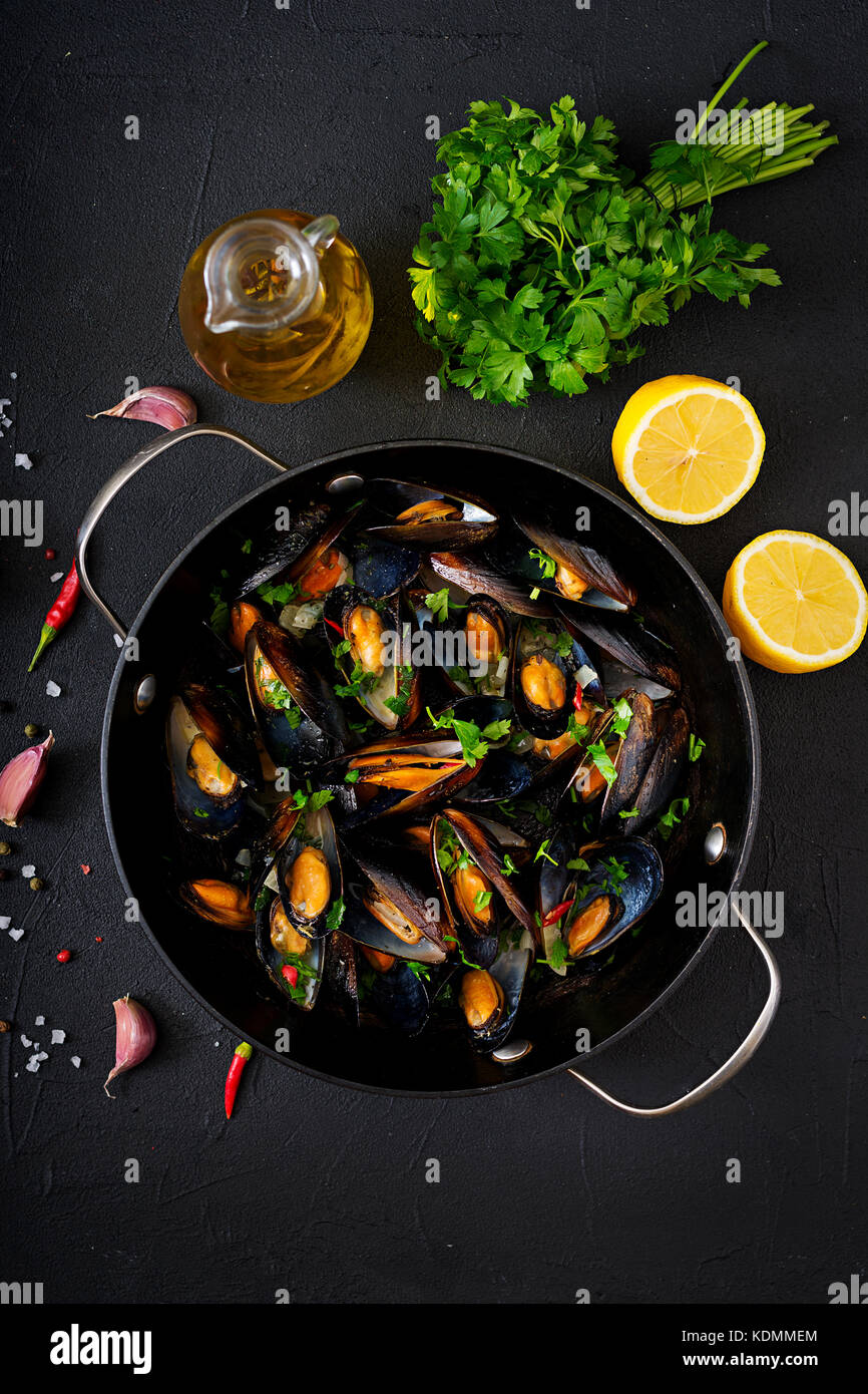 Mussels cooked in wine sauce with herbs in a frying pan on a black