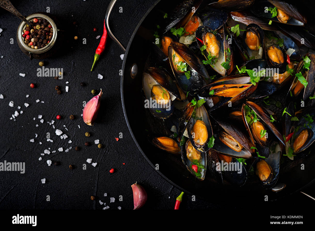 Mussels cooked in wine sauce with herbs in a frying pan on a black