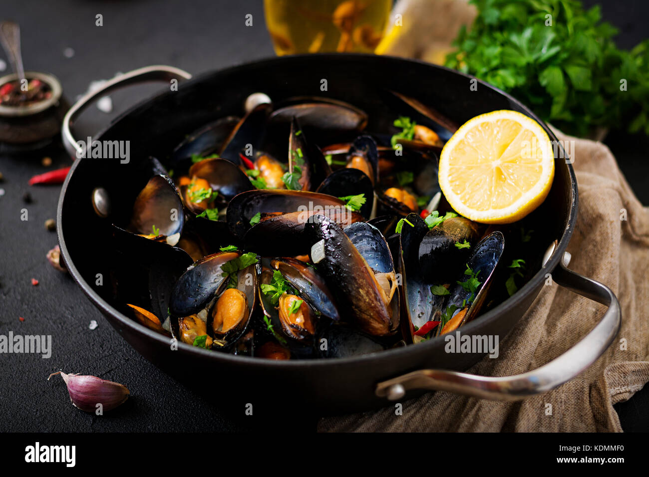 Mussels cooked in wine sauce with herbs in a frying pan on a black