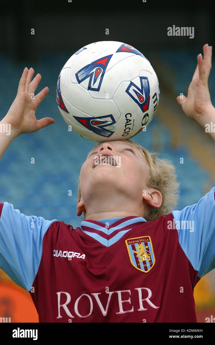 A young boy in an Aston Villa soccer shirt balances a football on his head Stock Photo