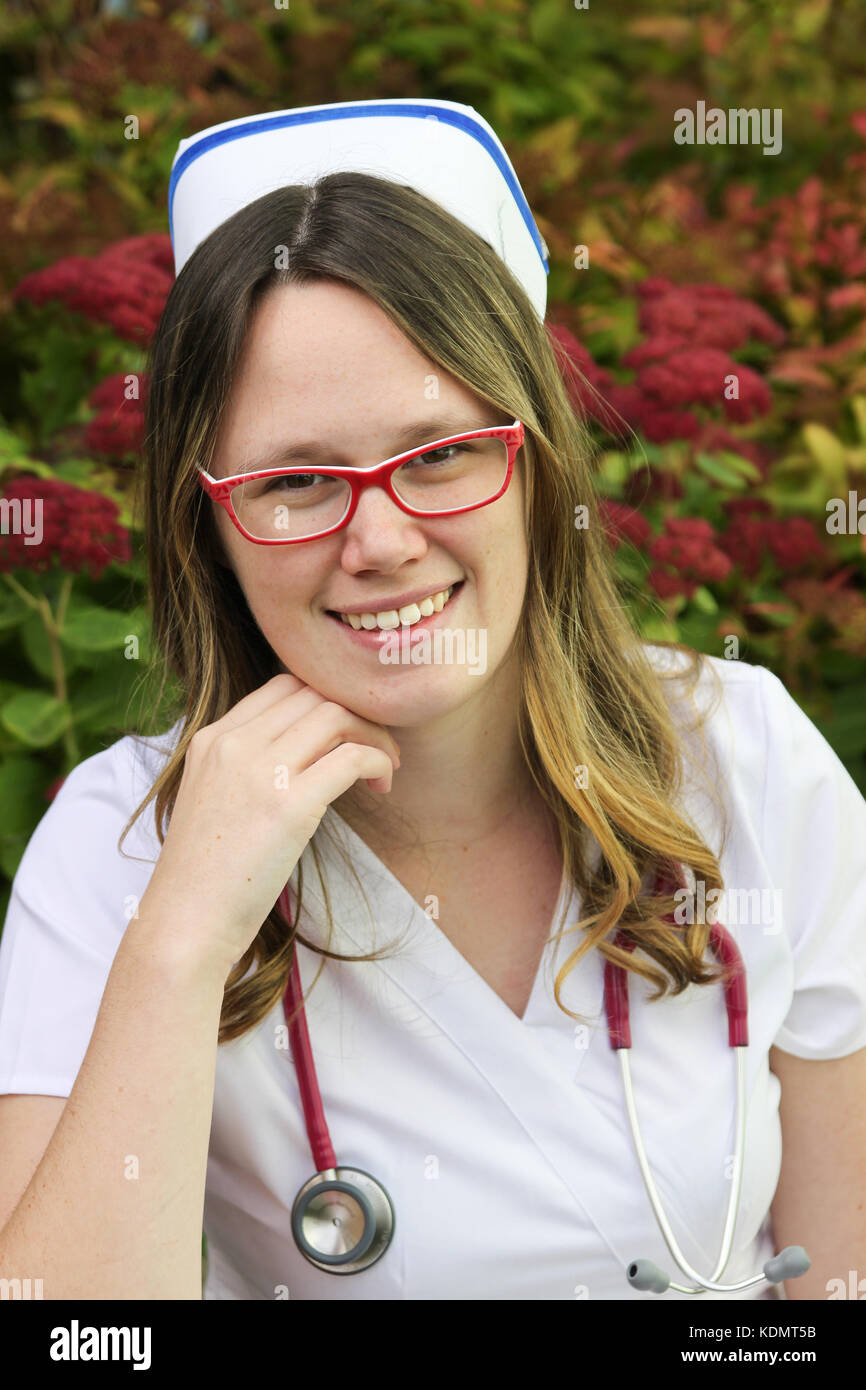 Young smiling female nurse portrait wearing white scrubs, cap and a stethoscope around her neck