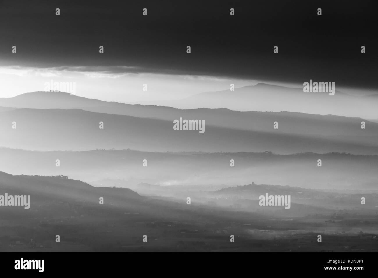 A valley filled by mist, with emerging hills and soft tones, beneath dark clouds Stock Photo