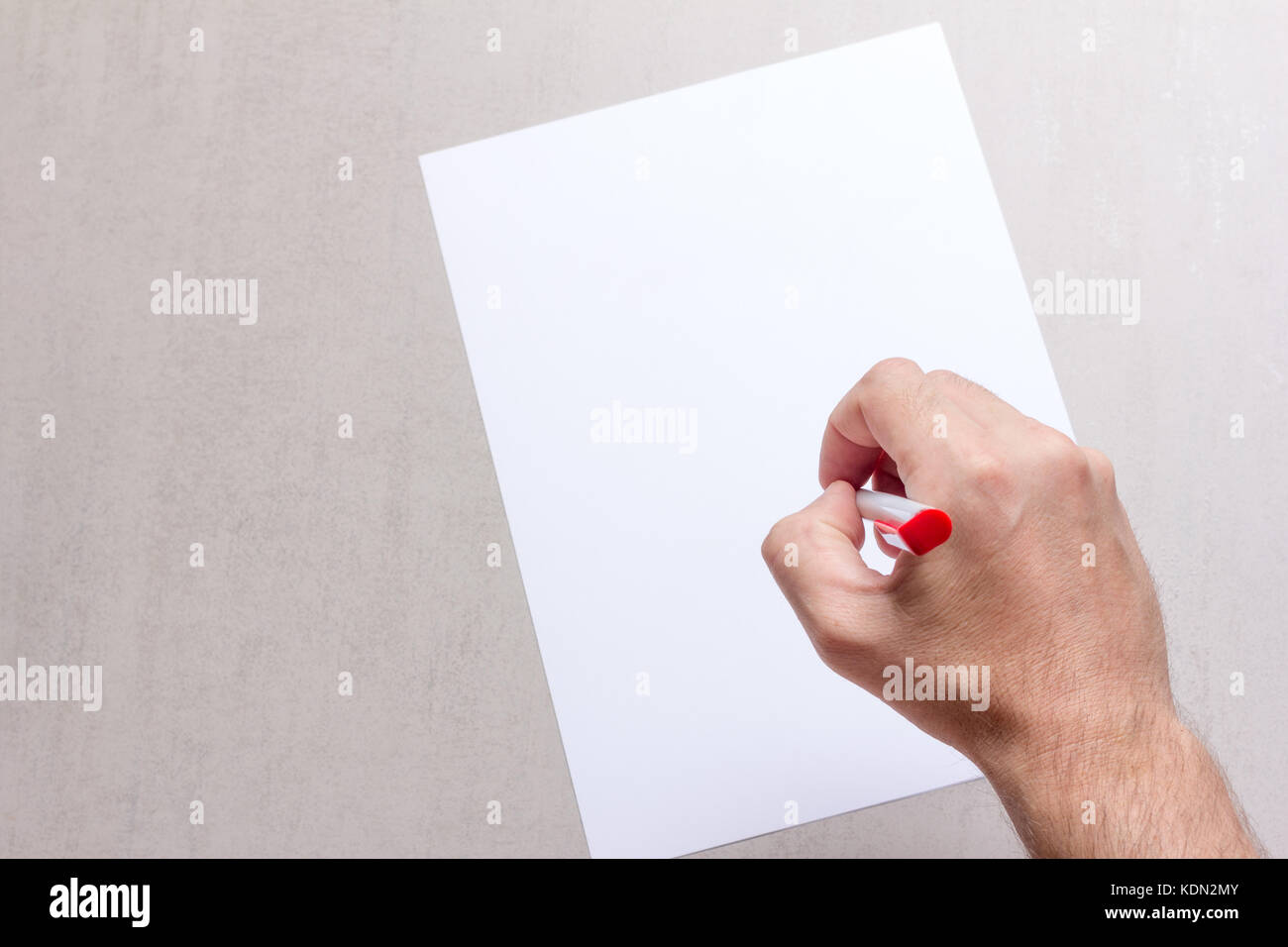 Mans hand with a ballpoint pen and blank white sheet of paper on a gray ...