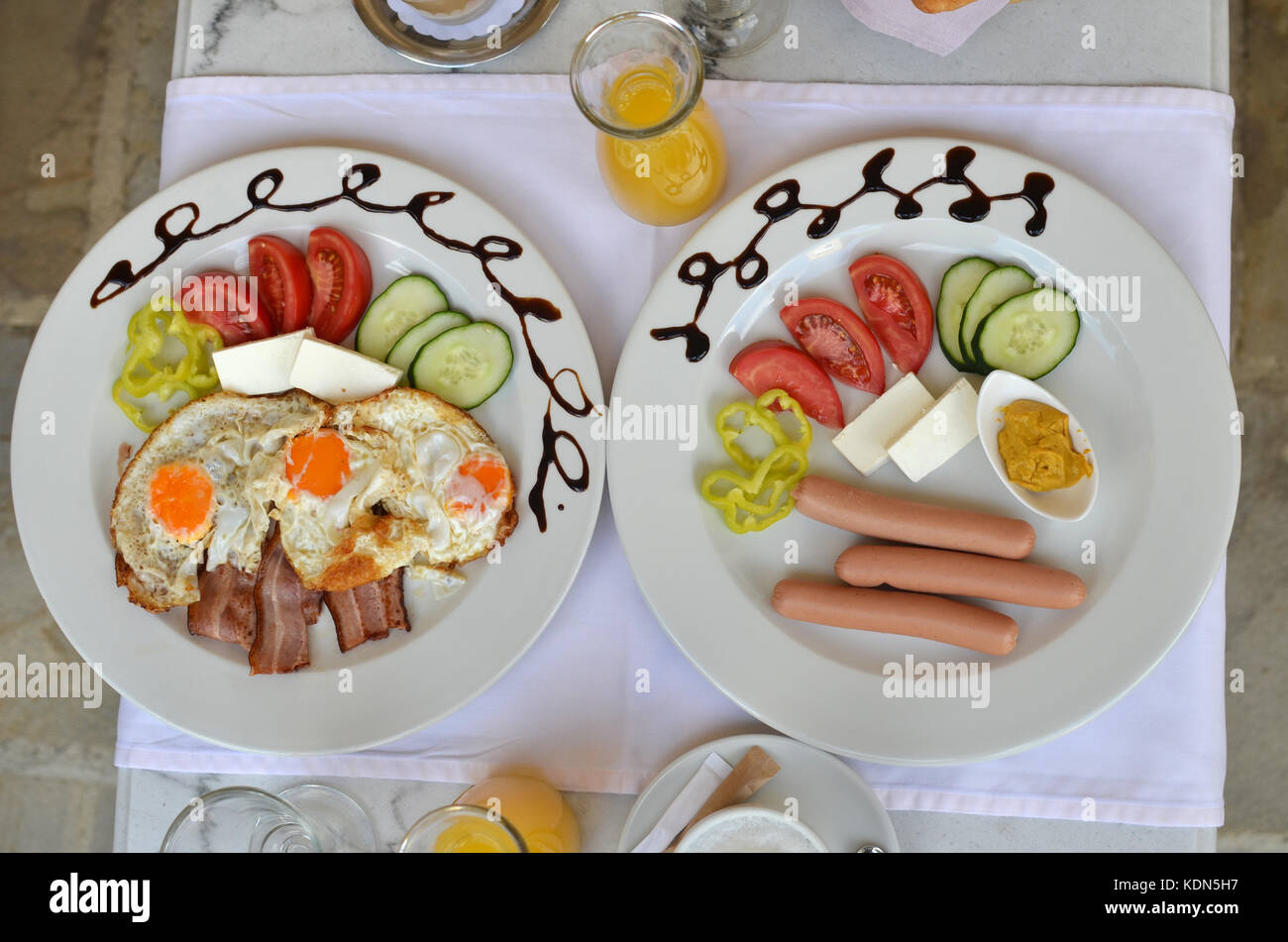 Plates with served breakfast - fried eggs, bacon, hot dogs and fresh vegetables Stock Photo