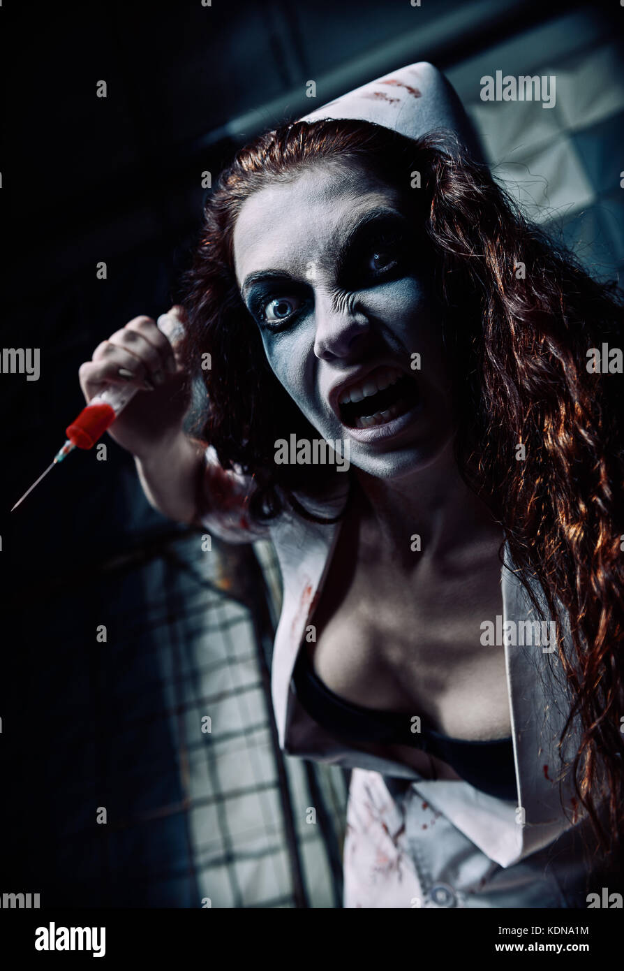 Horror shot: the crazy evil nurse (doctor) with syringe in hand. Zombie woman (living dead) Stock Photo