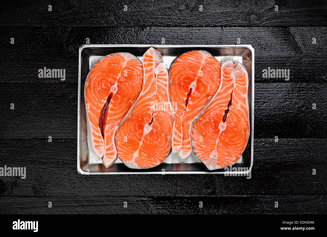 Salmon steaks on metal tray on black wooden table top view Stock Photo
