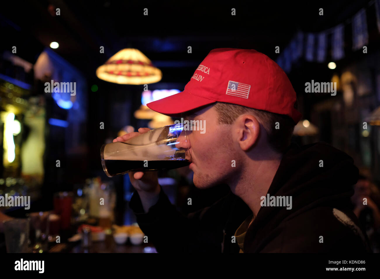 A young Israeli man drinking beer in a pub in Jerusalem and wearing the 'Make America Great Again' classic rope hat that Donald Trump used to wear during his campaign for presidency in the US. Stock Photo