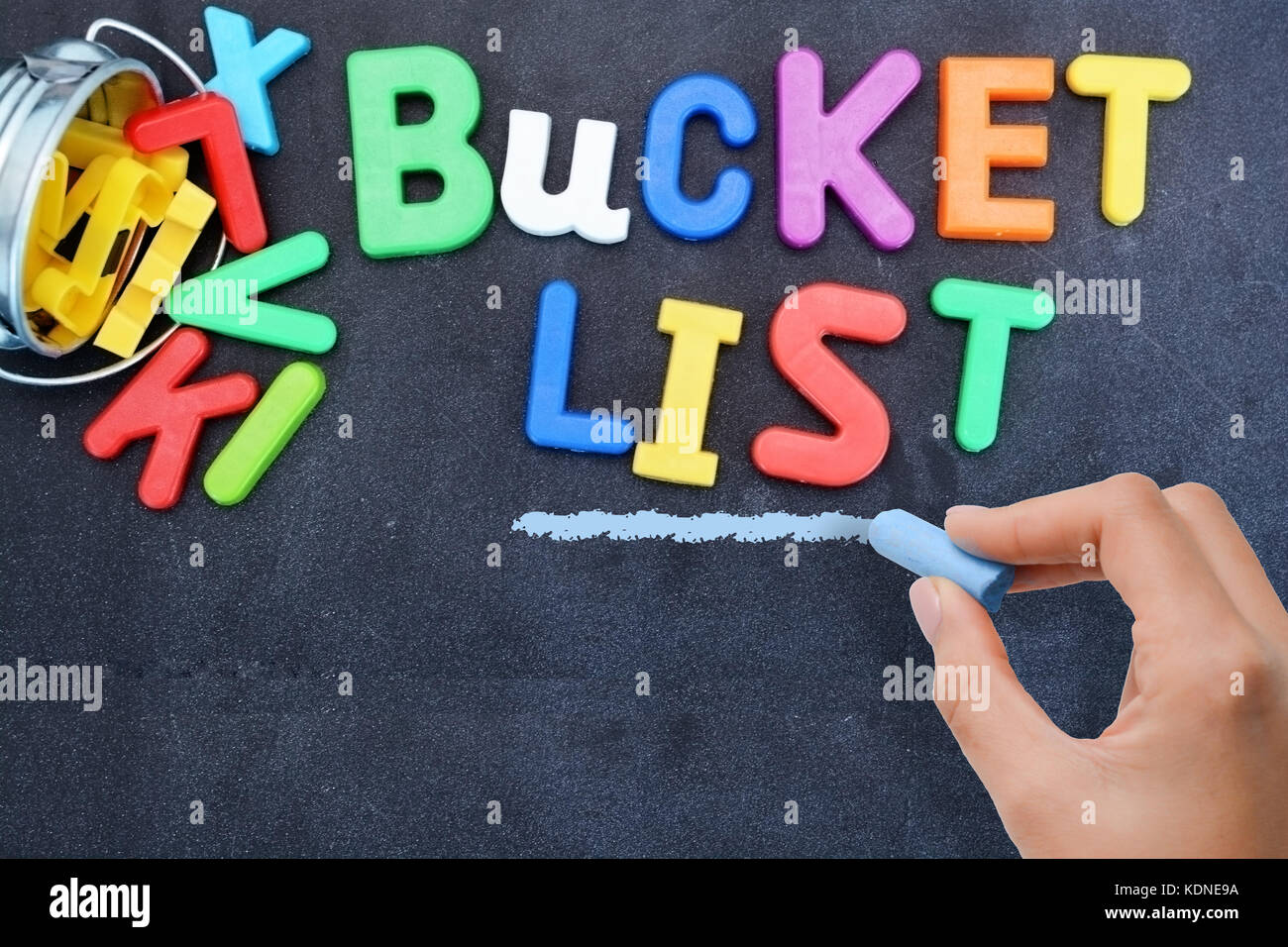 Young woman prepared for bucket list with metallic bucket and colorful plastic letters on blackboard Stock Photo