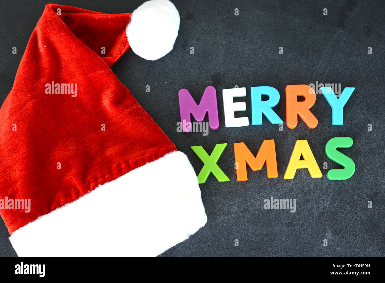 Merry Xmas colorful text with Santa’s red hat on dark background Stock Photo