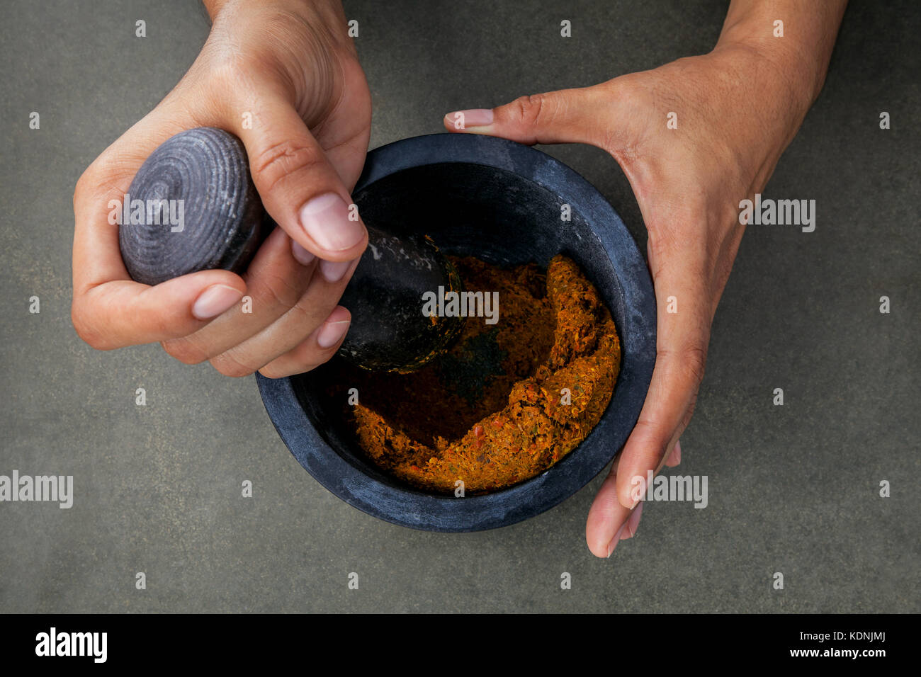 The women hold stone mortar with spice paste and pestle. Thai red paste