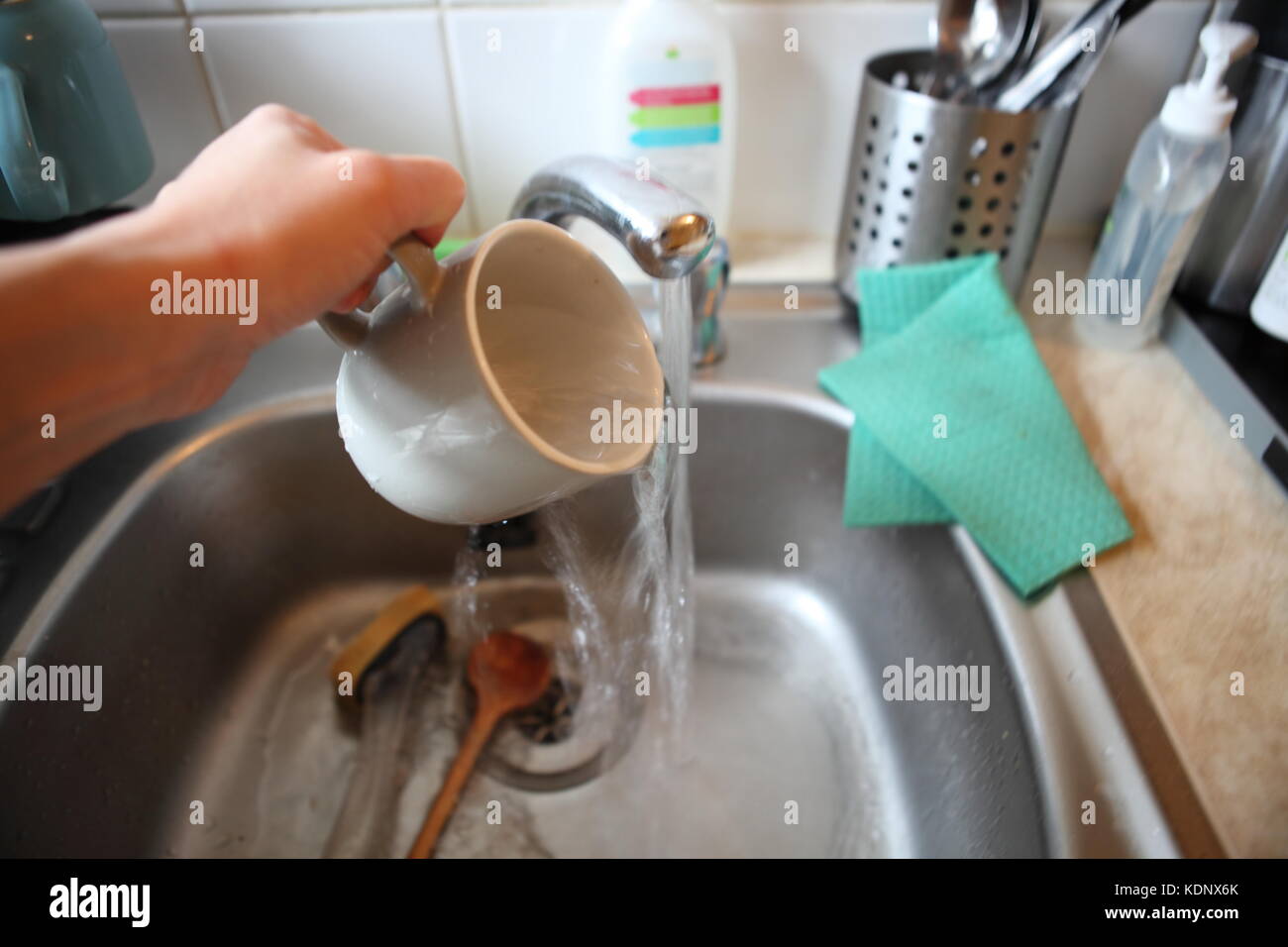 grey mug in metal washing up sink, with hand Stock Photo