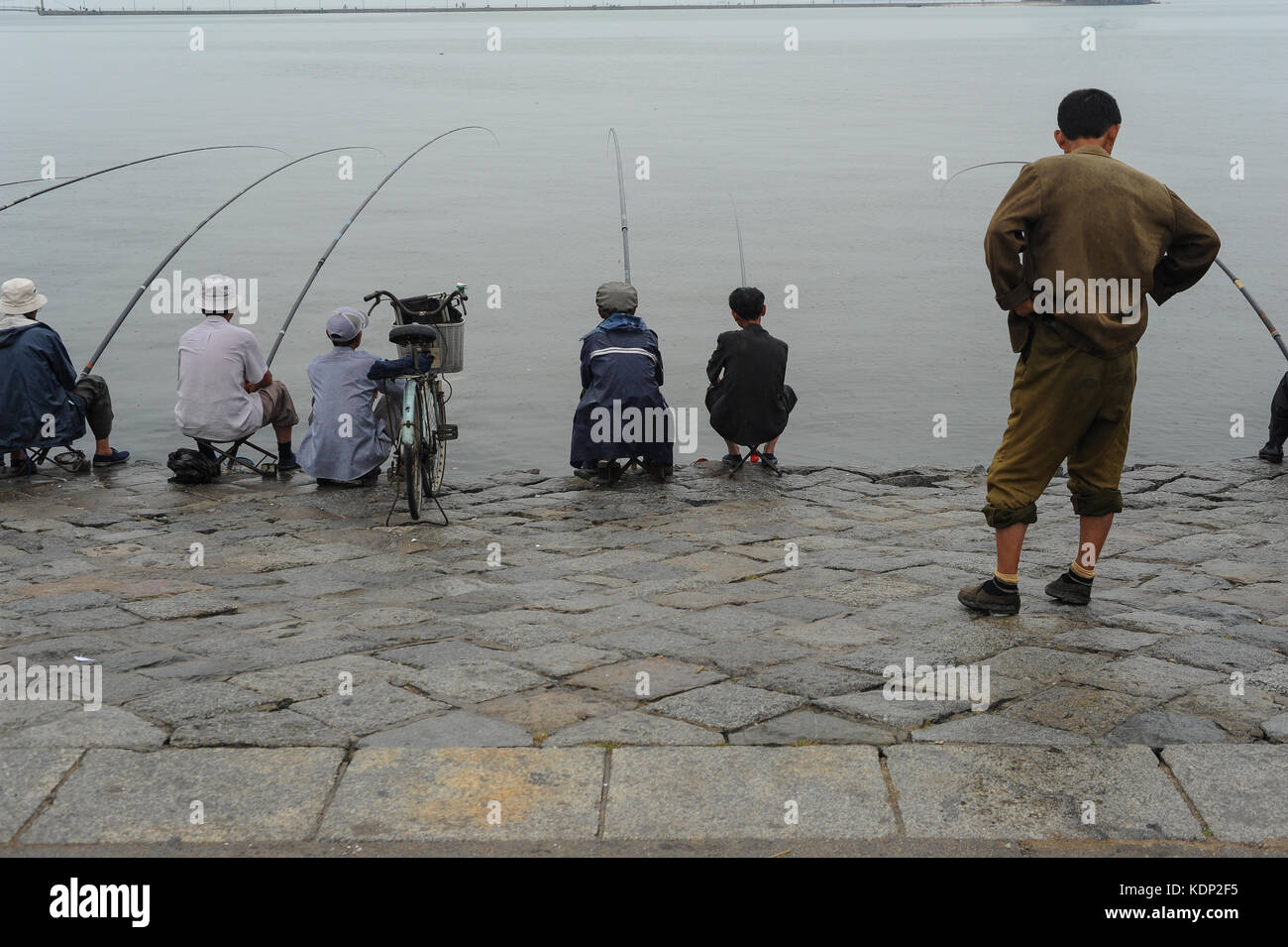 12.08.2012, Wonsan, North Korea, Asia - A North Korean man watches a group of locals fish on a grey and rainy morning in the coastal town of Wonsan. Stock Photo