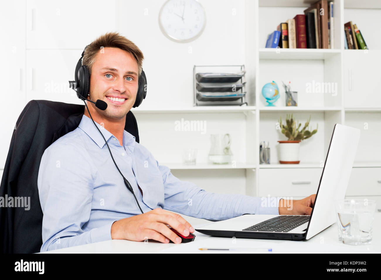 Smiling young man talking using hands-free set at customer service office Stock Photo