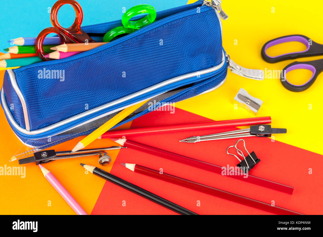 Blue pencil case full of colouring pencils and scissors on a colourful card background Stock Photo
