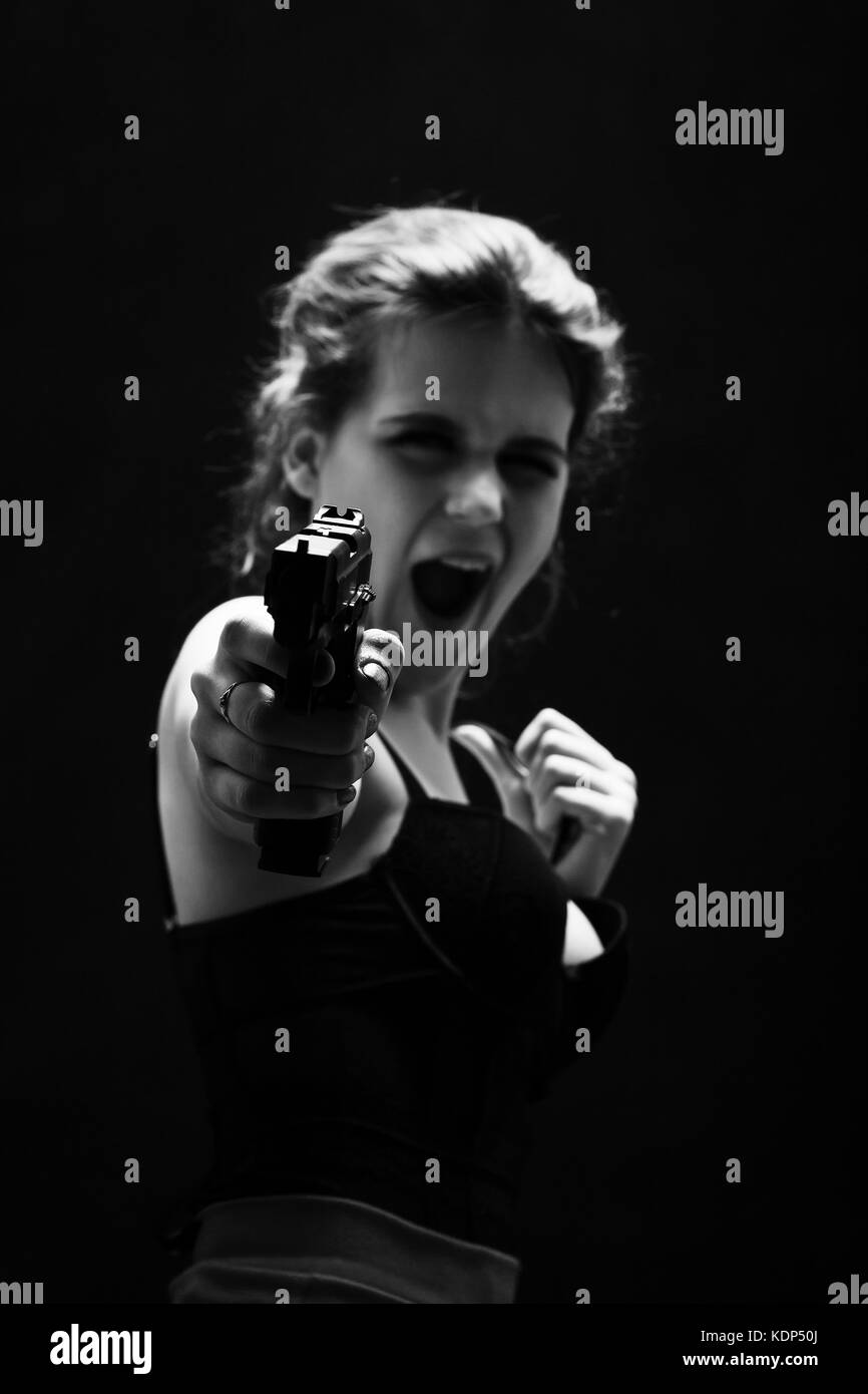 girl with gun on black background aiming at camera screaming, monochrome Stock Photo