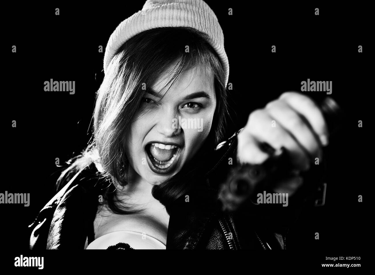 serious girl with gun on black background aiming at camera, screaming, monochrome Stock Photo