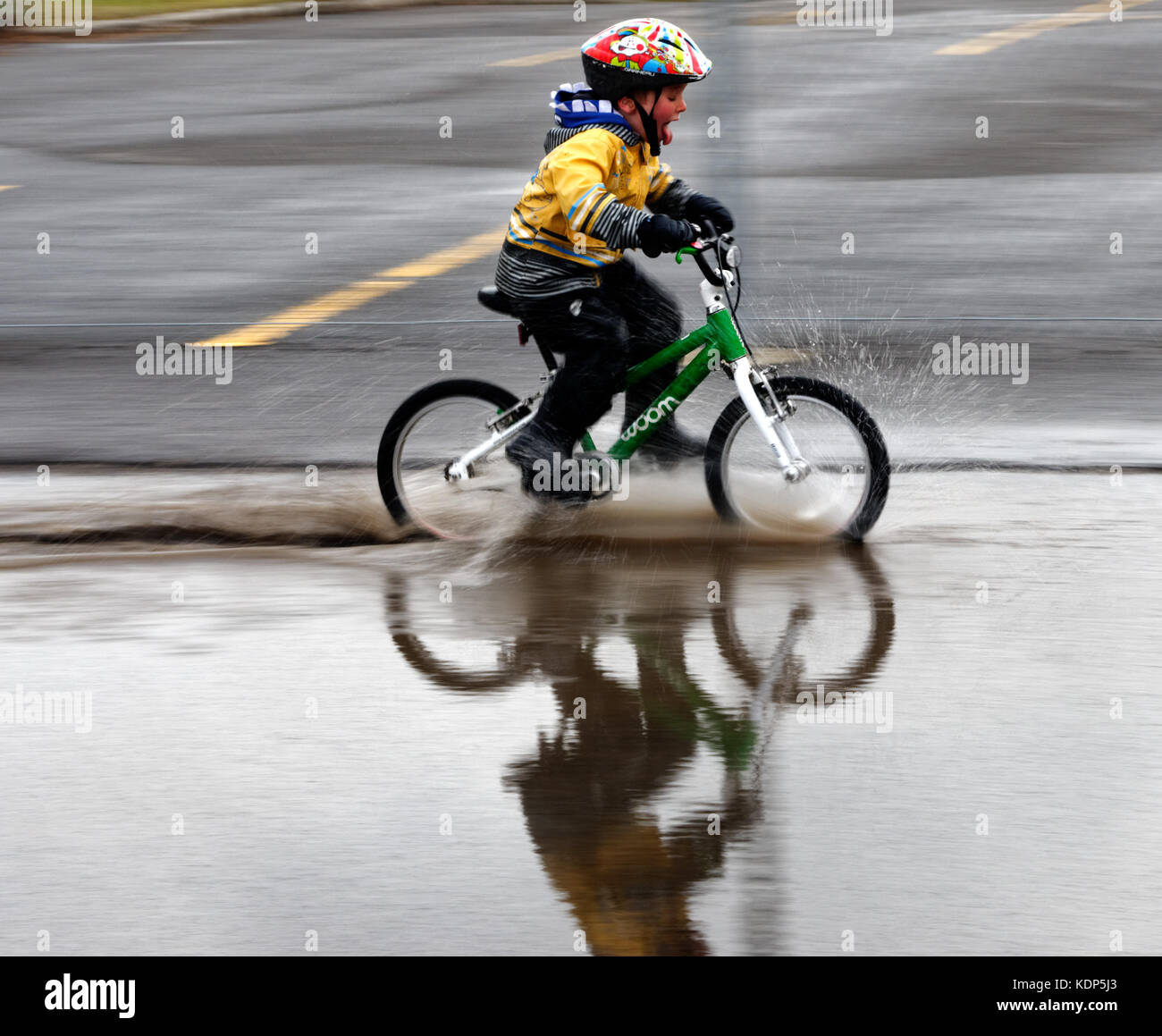 A little boy riding a bike through a big puddle Stock Photo