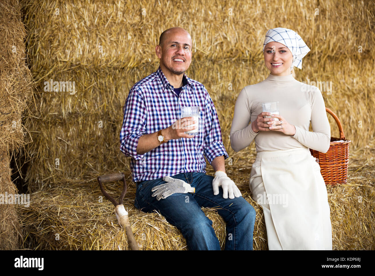Smiling two farmers,man and woman, taking pause with glass of milk in ...