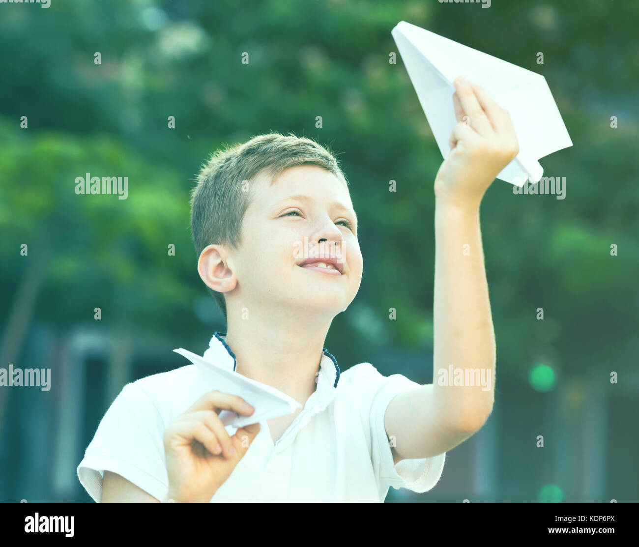 happy boy playing with simple paper airplane toy on sunny day in town ...